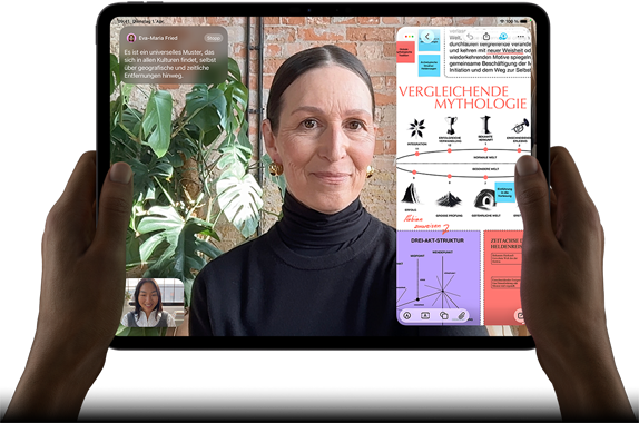 iPad Pro, Vorderansicht, Querformat, Farbe Space Schwarz, gerundete Ecken, schwarzer Displayrand, zwei Hände halten es an der linken und rechten Seite, das Display zeigt ein FaceTime Gespräch, das live übersetzt wird, und eine Lernapp zeigt eine Präsentation zum Thema „Vergleichende Mythologie“ mit Text, Diagrammen und handschriftlichen Notizen